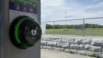 En hjertestarter henger på veggen foran et idrettsanlegg.