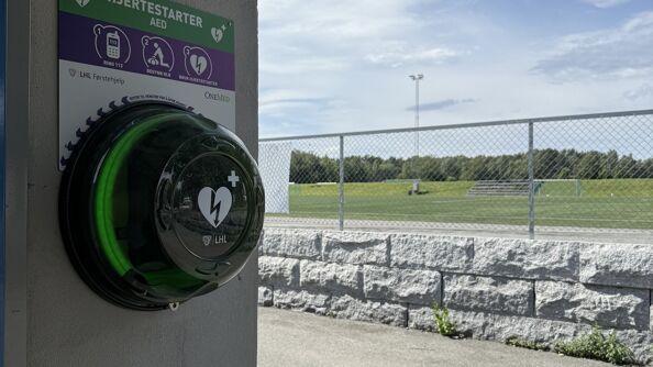 En hjertestarter henger på veggen foran et idrettsanlegg.