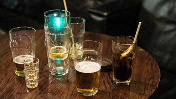 Bilde av halvfulle glass med drinker, øl og tomme shot-glass på et brunt bord.