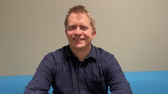 Mann med blondt hår og blå skjorte i lyseblå sofa.