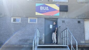 Bildet viser en mann som står på toppen av en trapp ved en dør. over døra henger et skilt der det står BUA Østensjø.