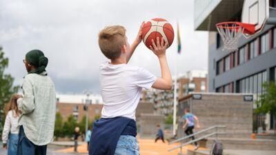 Ung gutt i hvit t-skjorte og blondt hår er i ferd med å kaste en basketball.