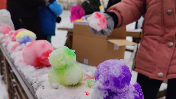 Snøballer med farger som ligger på rad. En person står med en snøball i hånda.