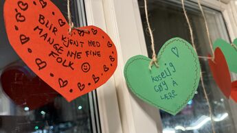Papirhjerter som henger i vinduet med tekst på.