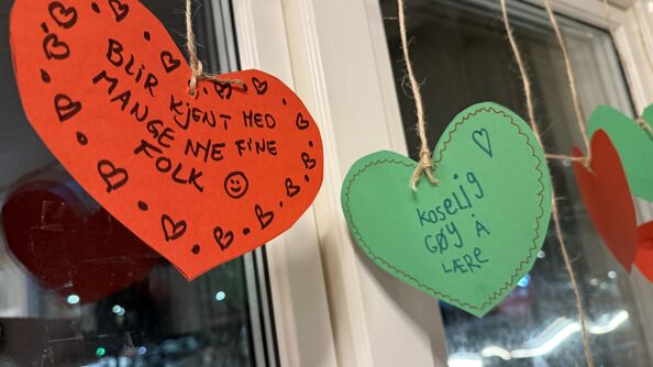 Papirhjerter som henger i vinduet med tekst på.