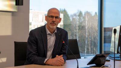 Bydelsdirektør sitter foran et skrivebord og ser i kamera