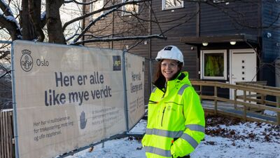 Kvinne i verneutstyr står foran et blått bygg, som er besøkssenteret til det nye Tøyenbadet.