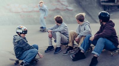Fire gutter sitter på en skateramp og ser på en annen gutt som ruller.