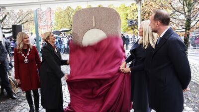 Fire prominente personer står rundt et monument i granittstein og trekker ned et vinrødt stykke stoff.