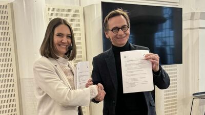 En kvinne og en mann tar hverandre i hendene samtidig som de holder opp en felles avtale.