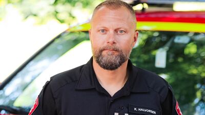 Mann i mørkeblå uniform foran rød og gul bil