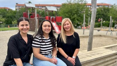 På bildet sitte ansatt i ambulant team Kine Sæther, pedagogisk leder Anna Marie Midtgård Ignacio og styrer Anne Christin Aastad på en benk foran en sandkasse i en barnehage.