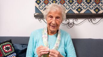 Eldre kvinne sitter i sofa og strikker