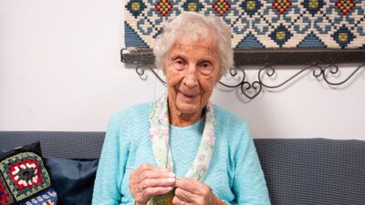 Eldre kvinne sitter i sofa og strikker