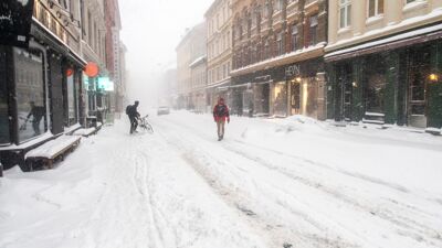 Snødekt Torggata med syklist som strever og fotgjenger som går i et bilspor.