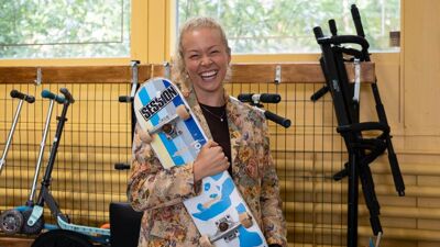 Kvinne med blomstrete jakke smiler med et skateboard i armene