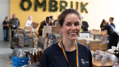 Kvinne smiler foran gul vegg hvor det står OMBRUK med store bokstaver