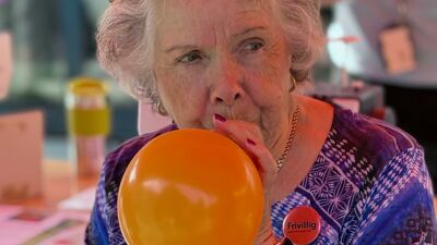Voksen kvinne som er frivillig ved St. Hanshaugen frivilligsentral blåser opp en orange ballong.