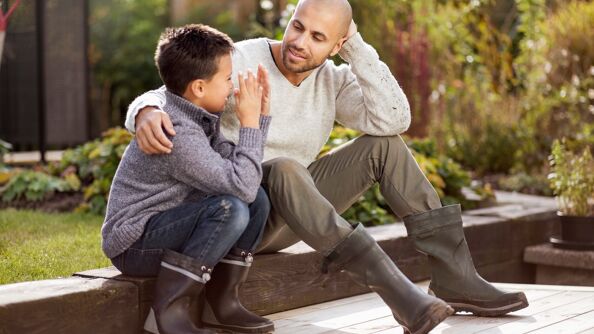 Far og sønn snakker sammen på en benk i hagen