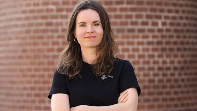 Kvinne i t-skjorte foran teglsteinsvegg med armene i kors.