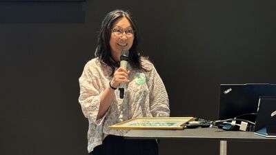 Ståernde kvinne snakker smilende i mikrofon bak et bord.