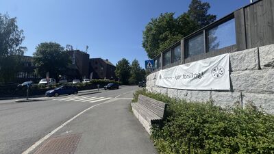 Banner på veggen i Slemdals-krysset med teksten "Skolevei - kjør forsiktig".