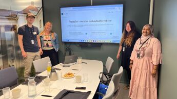 Fire representanter for bydelene deltar på workshop. De står rundt et bord og ser mot kamera mens de smiler.