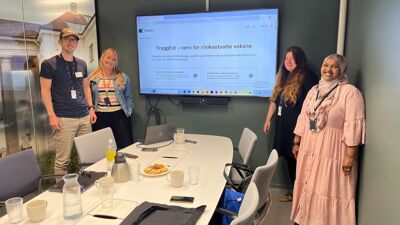 Fire representanter for bydelene deltar på workshop. De står rundt et bord og ser mot kamera mens de smiler.