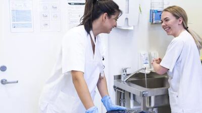 To helsearbeidere kledd i hvitt som smiler til hverandre