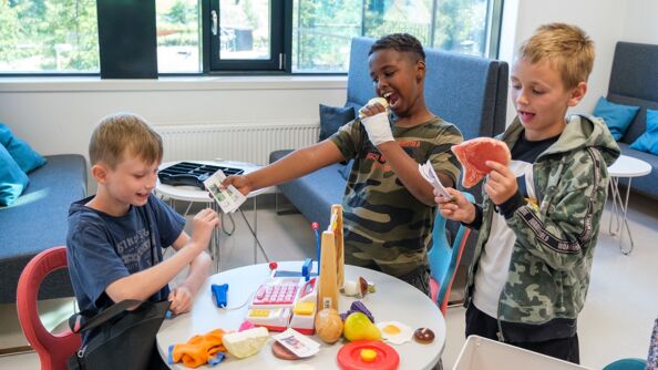 Tre skolegutter leker butikk med lekepepenger, kassaapparat, kuleramme og lekemat