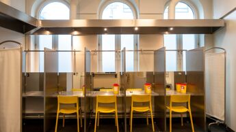 Innsiden av et rom: Fire stoler står med ryggen til, i hver sin avlukkede bås. Hver bås har bord, speil og bokser til brukt brukerutstyr.