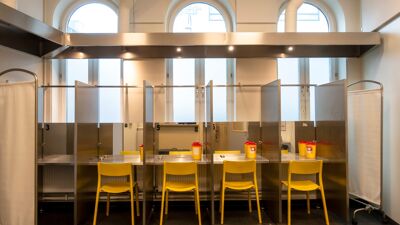 Innsiden av et rom: Fire stoler står med ryggen til, i hver sin avlukkede bås. Hver bås har bord, speil og bokser til brukt brukerutstyr.