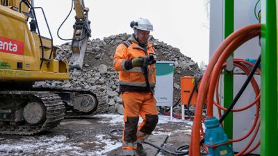 Mann som plugger i lader til gravemaskin på en byggeplass