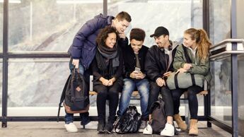 Ungdommer sitter samlet i et busskur. De er lent over en mobiltelefon.