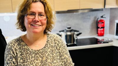 Kvinne med mønstret genser foran et bord. På bordet er det en gryte med linsesuppe og brød.
