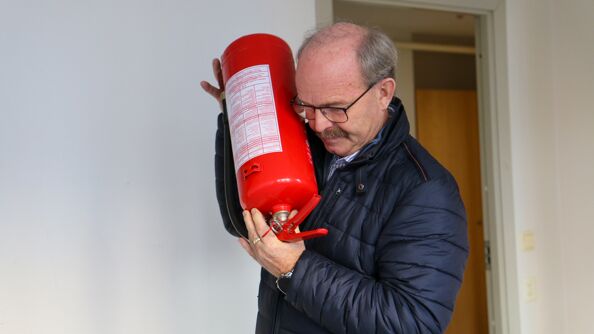 Brannvernrådgiver snur brannslukningsapparatet opp ned og hører etter om det rasler i pulveret inni.