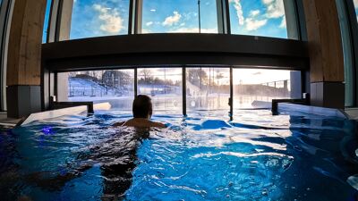 En person som svømmer i et oppvarmet basseng på det nye Tøyenbadet, med utsikt mot vinterlandskap og blå himmel gjennom store vinduer.