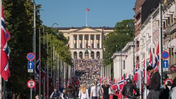 Karl Johan og Slottet. Mange mennesker og flagg på halv stang.