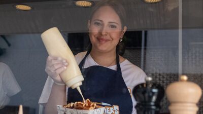 Smilende ungdomsskoleelev tar majones på maten som hun er i ferd med å selge.