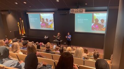 Byrådens står på scenen, med tegnespråktolk ved siden av seg, foran publium sittende i auditoriet.