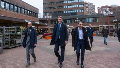Byråd for finans, byrådsleder og byråd for helse går på Tøyen torg med bygninger rundt dem.
