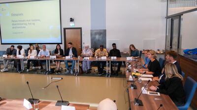 Mange mennesker samlet rundt bord i hestesko-oppsett i et stort møterom på rådhuset i Oslo.