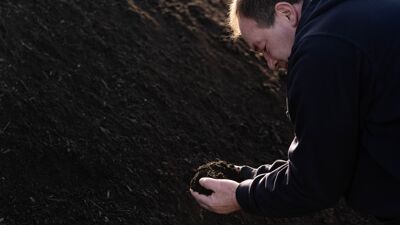 Mann bøyer seg ved jordhaug, med jord i hendene