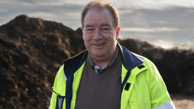 Mann med gul jakke foran jordhaug