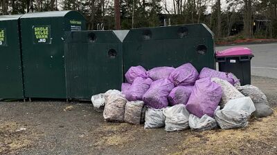 Hvite og lilla søppelsekker ved grønne containere