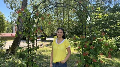 En kvinne i tskjorte og jeans står under en portal til parsellparken.