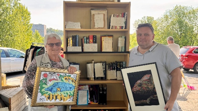 To personer står foran en bokhylle som de skal selge.