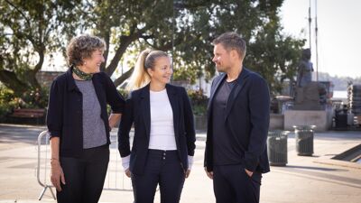 Programleder og to rektorer står sammen med Aker Brygge i bakgrunnen og smiler til hverandre.