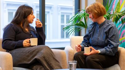 Hüsran og Åshild sitter i en sofa og drikker kaffe og prater