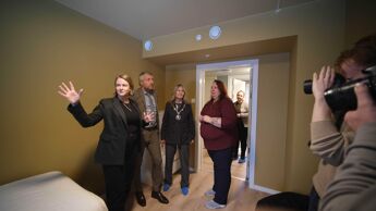 Fire mennsker står i et rom, de blir tatt bilde av av fortografer i bildekanten.